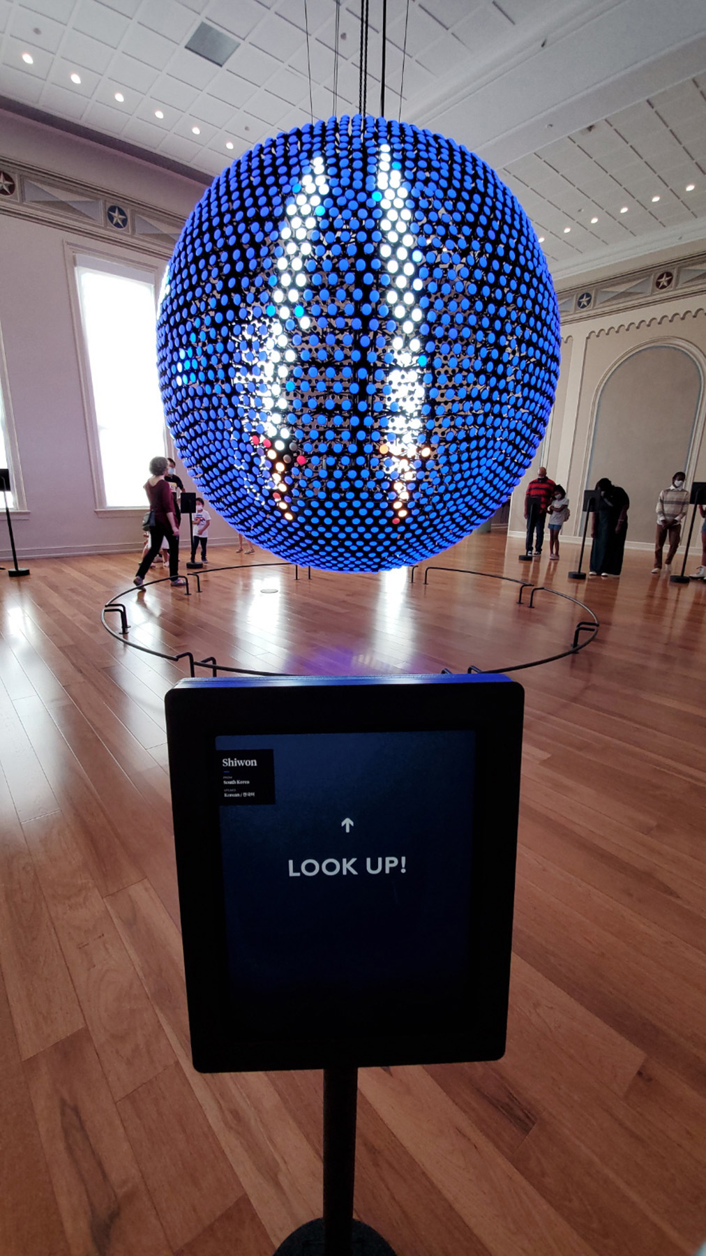 Almost exactly the same as the previous image, but this time the touch screen in the foreground simply has the words Look Up in the center with an arrow pointing to the top of the screen. The lights on the LED globe have changed; the land masses have disappeared and a graphic of two bright white swords surrounded by blue has replaced them.